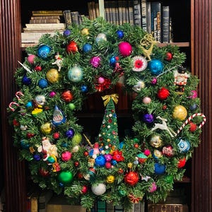 以下が含まれることがあります： 様々な色やサイズのクリスマスオーナメントで飾られた大きな人工の常緑樹のリース。球体のオーナメント、くるみ割り人形、サンタクロースのフィギュア、白い鹿、キャンディケイン、そして中央に小さなクリスマスツリーが装飾されています。
