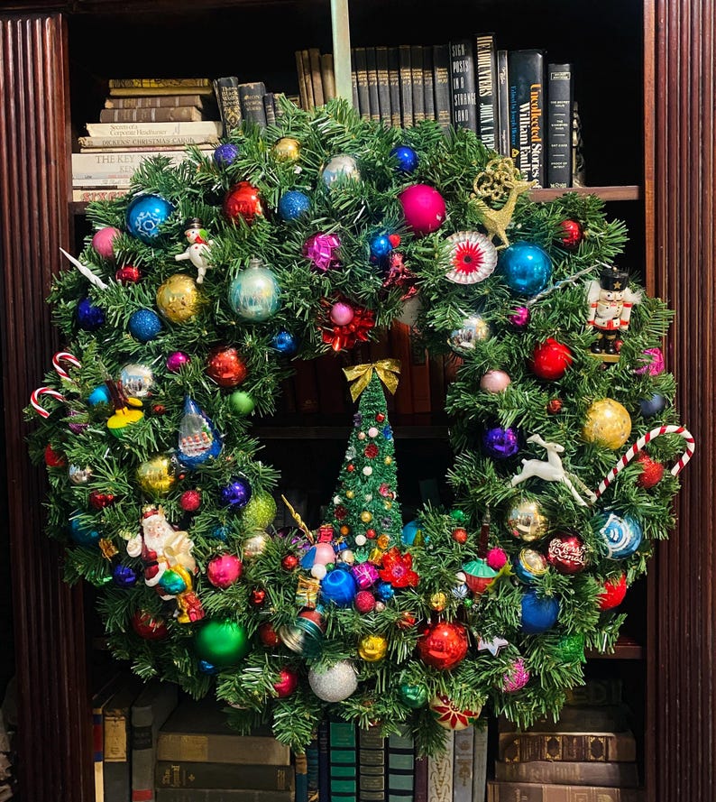 以下が含まれることがあります： 様々な色やサイズのクリスマスオーナメントで飾られた大きな人工の常緑樹のリース。球体のオーナメント、くるみ割り人形、サンタクロースのフィギュア、白い鹿、キャンディケイン、そして中央に小さなクリスマスツリーが装飾されています。