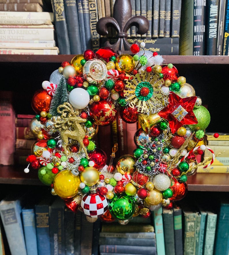 以下が含まれることがあります： 赤、緑、金、白の様々なサイズのオーナメントで構成された装飾的なホリデーリース。リースには、金色のグリッターで飾られたトナカイ、ミニチュアのボトルブラシツリー、赤い星、そしてMerry Christmasと書かれた金色のサインがあしらわれています。