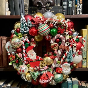 以下が含まれることがあります： 赤、緑、金のオーナメント、ミニチュアのクリスマスツリー、キャンディケイン、サンタクロースのフィギュア、トナカイを引くそり、NOELと書かれた看板で飾られたクリスマスリース。リースには様々な祝祭的な装飾が施されています。