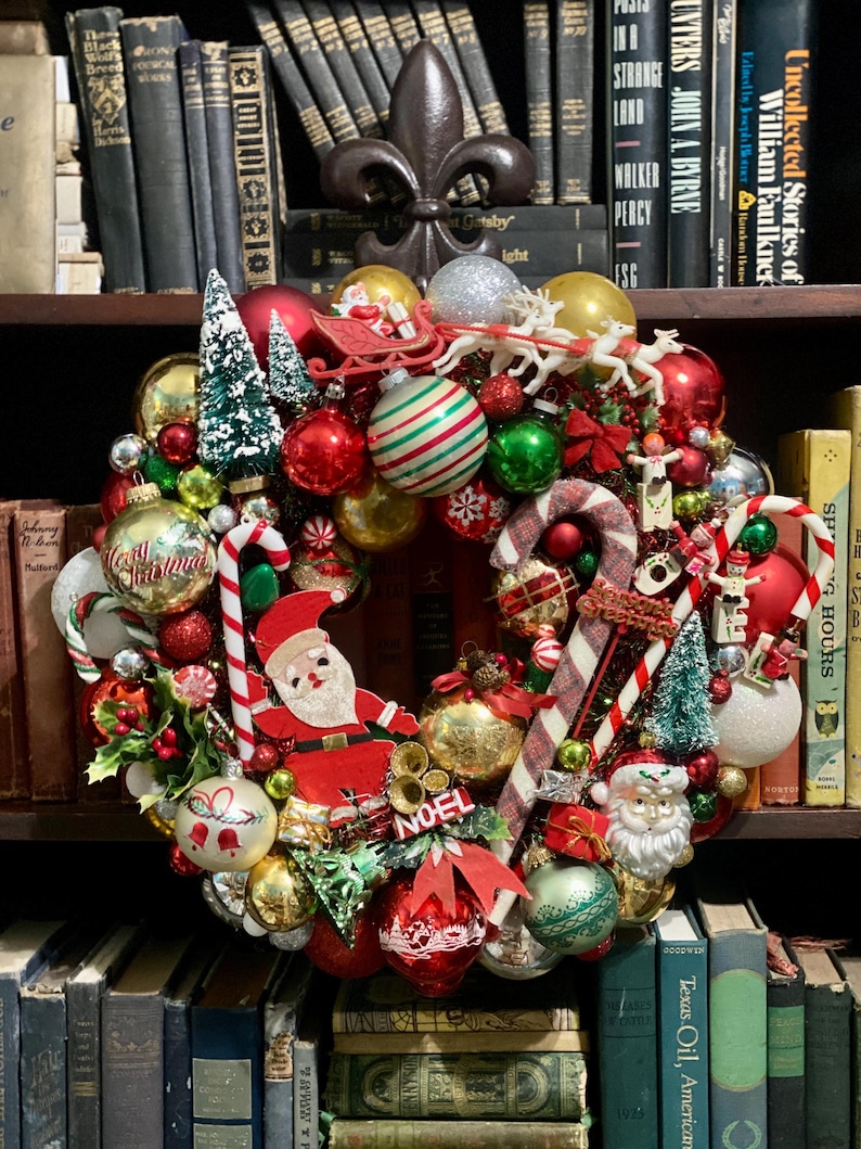 以下が含まれることがあります： 赤、緑、金のオーナメント、ミニチュアのクリスマスツリー、キャンディケイン、サンタクロースのフィギュア、トナカイを引くそり、NOELと書かれた看板で飾られたクリスマスリース。リースには様々な祝祭的な装飾が施されています。