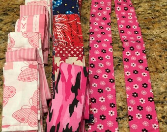 May include: A collection of pink and white fabric strips with various patterns, including butterflies, stripes, and flowers. There are also two long pink fabric strips with a white flower pattern.