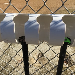 May include: White PVC pipe with cutouts for holding baseball bats. Two bats are in the holders, one with a black grip and a green grip.