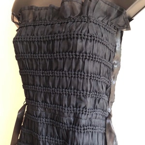 May include: A black strapless dress with a ruffled neckline and a gathered bodice. The dress has a black ribbon tie at the side.