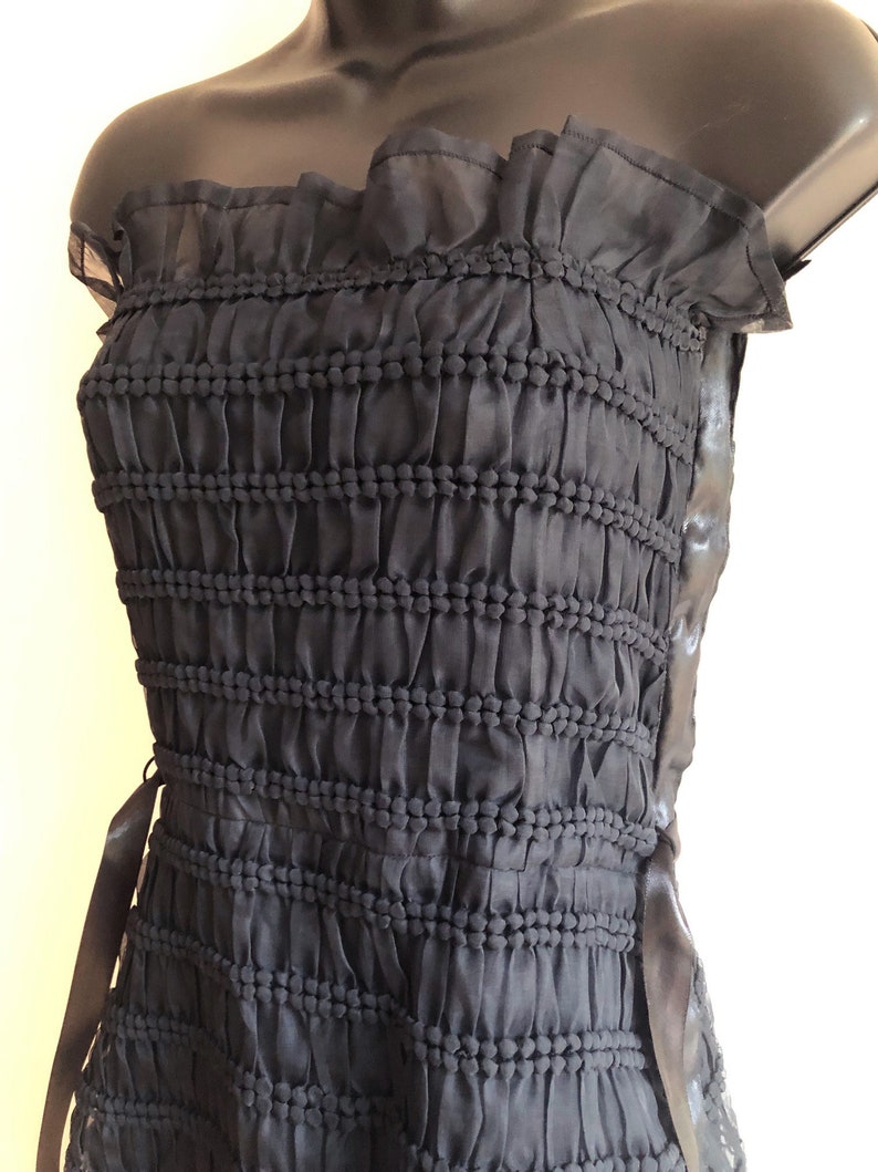 May include: A black strapless dress with a ruffled neckline and a gathered bodice. The dress has a black ribbon tie at the side.