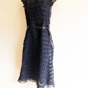 May include: A black strapless dress with a ruffled neckline and a black ribbon belt. The dress is made of a textured fabric and has a flowing skirt.