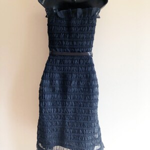 May include: A black strapless dress with a ruffled neckline and a black belt. The dress is made of a textured fabric and has a ruffled hem.
