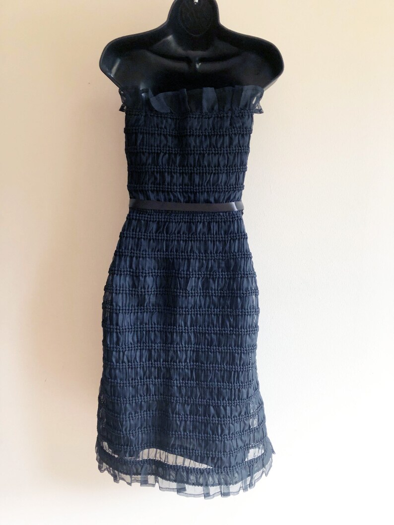 May include: A black strapless dress with a ruffled neckline and a black belt. The dress is made of a textured fabric and has a ruffled hem.