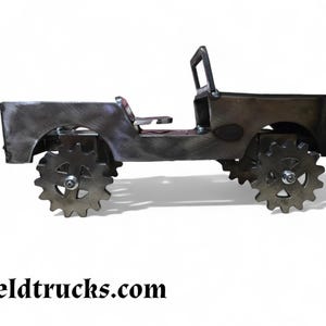 Op de afbeelding: Een metalen model van een Jeep met een zwarte afwerking en tandwielvormige wielen. Het model is gemaakt van gelast metaal en heeft een eenvoudig, rustiek ontwerp.