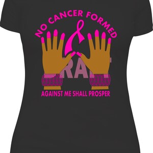 May include: Black t-shirt with a pink graphic design. The design includes the text "NO CANCER FORMED AGAINST ME SHALL PROSPER" and a pink ribbon. The graphic also features two hands with pink fingernails and bracelets.