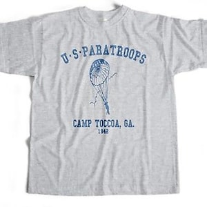 May include: A gray t-shirt with a blue print of a paratrooper and the text "U.S. PARATROOPS CAMP TOCCOA, GA. 1942".