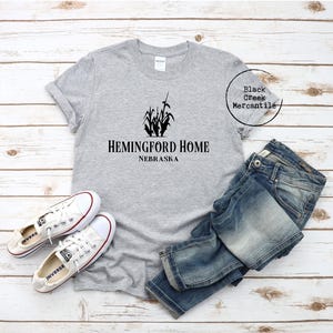 May include: Gray t-shirt with a black graphic of corn stalks and the text "Hemingford Home Nebraska".