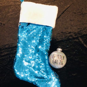 May include: A blue sequin Christmas stocking with a white faux fur cuff and a silver glitter ornament that says "Glitter Gal 716".
