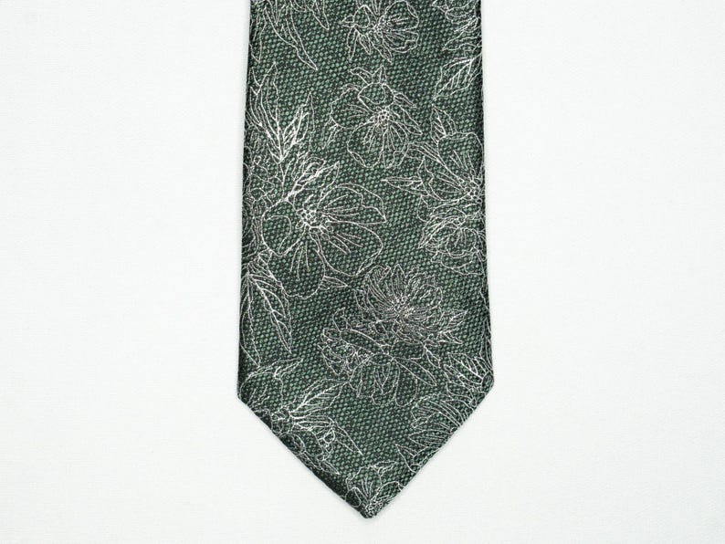 May include: A dark green necktie with a floral pattern. The tie features a repeating design of white floral outlines against a textured background. The tie is displayed against a white background.