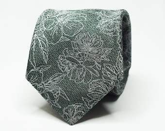 Könnte beinhalten: Eine dunkelgrüne Krawatte mit floralem Muster. Die Krawatte zeigt ein sich wiederholendes Design aus weißen Blumen und Blättern. Der Stoff hat eine strukturierte Optik, und die Krawatte ist geknotet, was ihr Design hervorhebt.