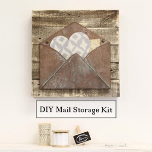 May include: DIY mail storage kit with a rustic wooden frame and a metal envelope with a distressed finish. The envelope has a heart-shaped opening and is decorated with a patterned fabric.
