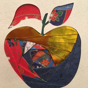 May include: A paper craft apple with a red, gold, blue, and white patterned design. The apple has a green stem and two leaves.