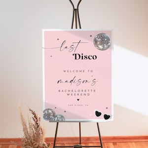 Puede incluir: Un cartel rosa para una despedida de soltera con el texto "last disco" y "welcome to madison's bachelorette weekend" con una bola de discoteca y gafas de sol. El cartel est&aacute; en un caballete negro.