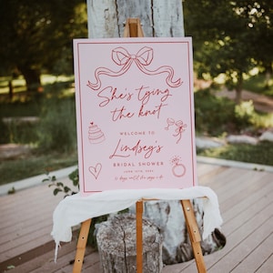 Letrero de bienvenida para despedida de soltera "She's Tying The Knot", lazo rosa, rosa y rojo, dibujado a mano, caprichoso, editable e imprimible, coqueto.