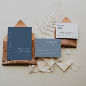 May include: A blue invitation card with white text for a baby shower in honor of Madison James. The invitation includes the date, time, and location of the event. There are also two smaller cards, one for a diaper raffle and one for a book drive for the baby.