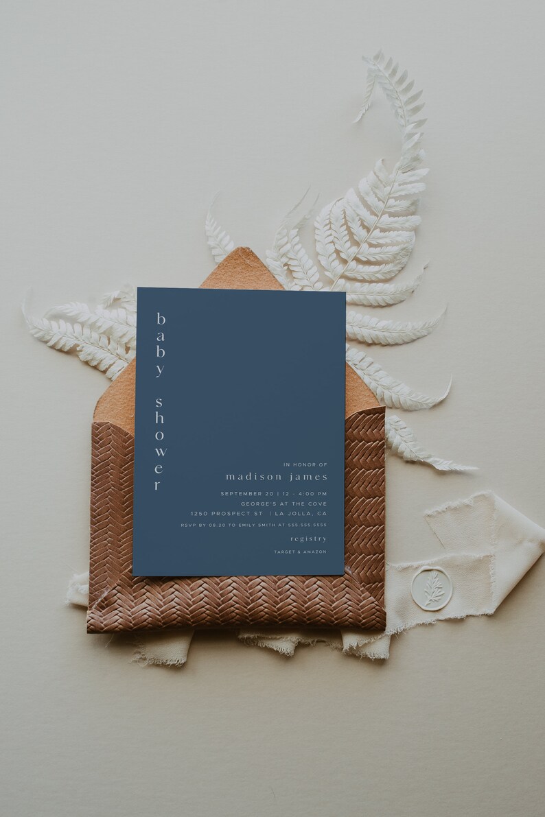 May include: A blue baby shower invitation with white text. The invitation reads "baby shower" vertically on the left side and "in honor of madison james" at the top. The invitation includes the date, time, location, RSVP information, and registry details.