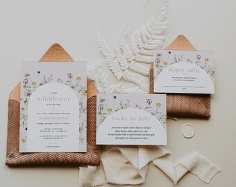 May include: A baby shower invitation suite with a floral design. The suite includes an invitation, a diaper raffle card, and a books for baby card. The cards are placed in woven brown envelopes and decorated with white fern and ribbon.