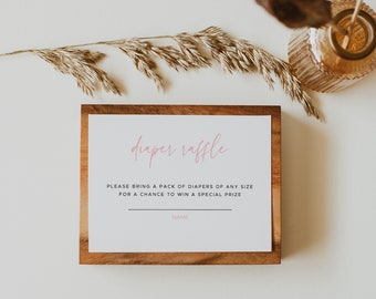 May include: A wooden sign with a white card insert that says "diaper raffle" in pink script. The text below reads "Please bring a pack of diapers of any size for a chance to win a special prize." There is a blank line for a name.