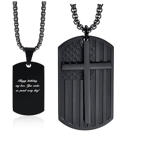 May include: Black stainless steel necklace with two pendants. One pendant is a dog tag with an American flag and a cross design. The other pendant is a dog tag with the text "Happy birthday my love. You make us proud every day!"