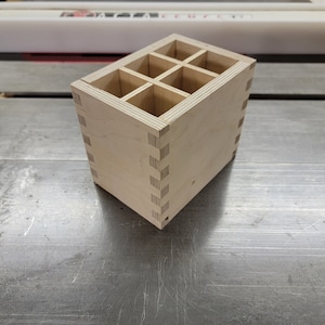 May include: A wooden organizer with nine compartments, made of light-colored wood with a natural finish. The organizer has a simple, rectangular design and is perfect for storing small items.