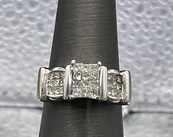 May include: A silver ring with a square-shaped diamond center stone and smaller diamonds surrounding it.