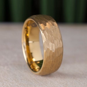 May include: A gold-toned hammered tungsten carbide ring. The ring has a brushed finish and a wide band.