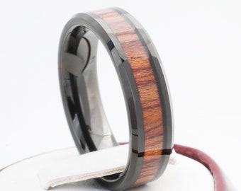 Puede incluir: Un anillo de carburo de tungsteno negro con una banda de incrustación de madera de Koa. El anillo tiene un borde biselado y un acabado pulido.