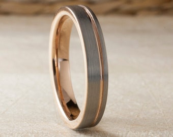 May include: A two-tone ring with a brushed gray exterior and a rose gold interior. A thin rose gold stripe runs down the center of the gray band. The ring is set against a neutral background.