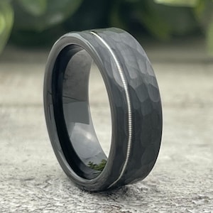 May include: A black tungsten carbide ring with a hammered finish and a thin silver line inlay.
