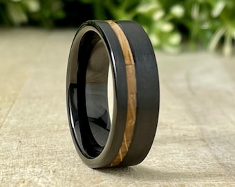 May include: A black tungsten carbide ring with a brown wood inlay. The ring is polished and has a smooth finish.