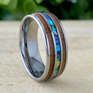 May include: A silver tungsten carbide ring with a brown wood inlay and a blue and green abalone shell inlay.