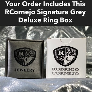 Puede incluir: Una caja de anillo gris con un logotipo en blanco y negro que dice "RCornejo Joyer&iacute;a". La caja est&aacute; cerrada y tiene una etiqueta blanca en el lateral que dice "Rodrigo Cornejo".