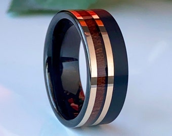 May include: A black tungsten carbide ring with two thin bands of wood inlay. The wood is a dark brown color with a reddish hue.