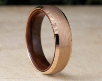 May include: A rose gold tungsten carbide ring with a brushed finish and a wooden inlay. The ring is approximately 8mm wide.