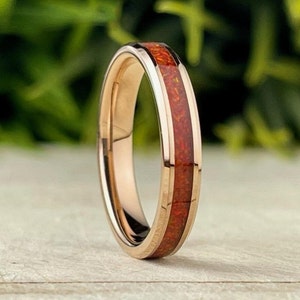 May include: A rose gold tungsten carbide ring with a red and gold inlay. The ring is a simple band with a thin inlay of red and gold.