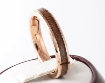 May include: Rose gold ring with a dark brown wood inlay. The ring is set against a white background, showcasing the polished metal and the natural wood grain. A close-up shot highlights the ring's design.