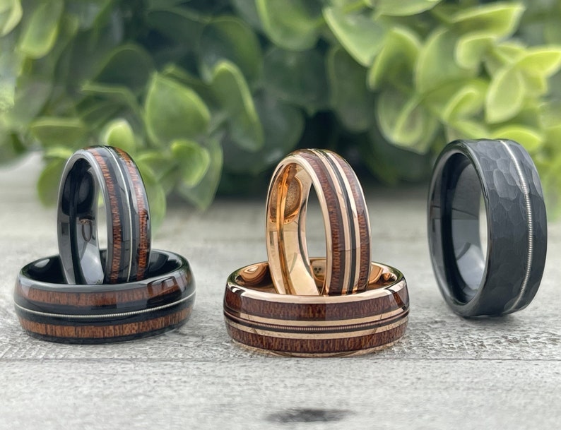 Pode incluir: Tr&ecirc;s alian&ccedil;as de casamento para homem com estilos diferentes. Uma banda &eacute; preta com acabamento martelado, outra &eacute; preta com incrusta&ccedil;&atilde;o de madeira e a terceira &eacute; de ouro rosa com incrusta&ccedil;&atilde;o de madeira.