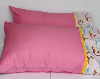 May include: Two pink pillowcases, one with a plain pink front and the other with a pink and white unicorn and rainbow print on the back.