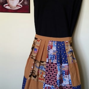 May include: A brown and tan patchwork apron with red, white, and blue stars and patriotic designs. The apron has a pleated skirt and a black waistband.