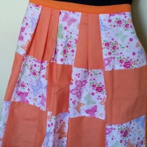 May include: A patchwork apron with a peach background and a white and pink floral print with butterflies. The apron has a peach colored waistband.
