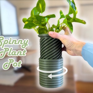 May include: A green plant pot with a spinning base. The pot is made of a textured material and has a dark green color. The text "Spinny Plant Pot" is written in green on a white background.