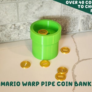 May include: A green plastic Mario warp pipe coin bank with gold coins inside and scattered around it. The text "OVER 40 COLORS TO CHOOSE FROM" is in the top right corner of the image. The text "MARIO WARP PIPE COIN BANK" is at the bottom of the image.