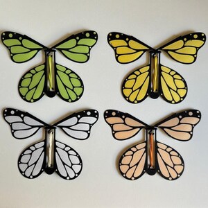 May include: Four butterfly-shaped toys with black outlines and different colored wings. The wings are green, yellow, white, and peach.
