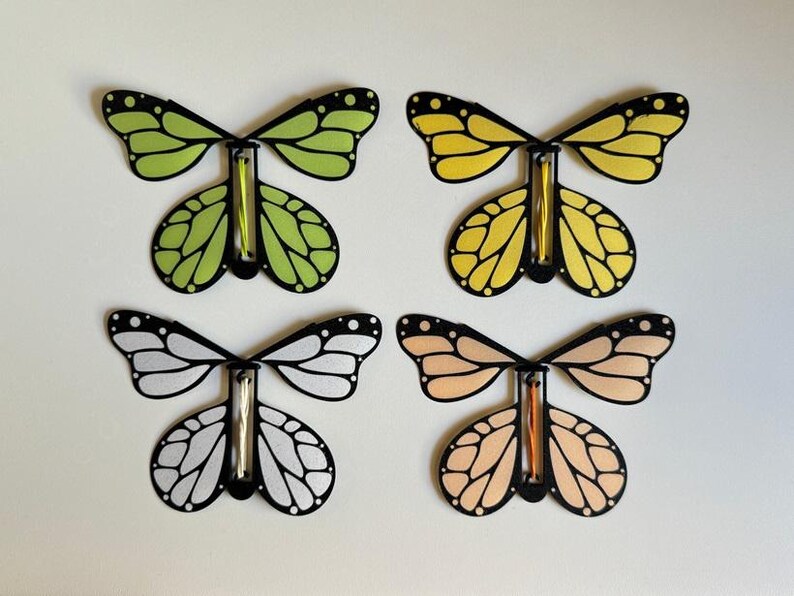 May include: Four butterfly-shaped toys with black outlines and different colored wings. The wings are green, yellow, white, and peach.