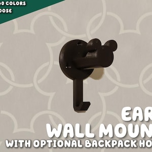 May include: Black plastic wall mount shaped like Mickey Mouse ears with a hook for hanging items. The text "EARS WALL MOUNT WITH OPTIONAL BACKPACK HOOK" is below the image.